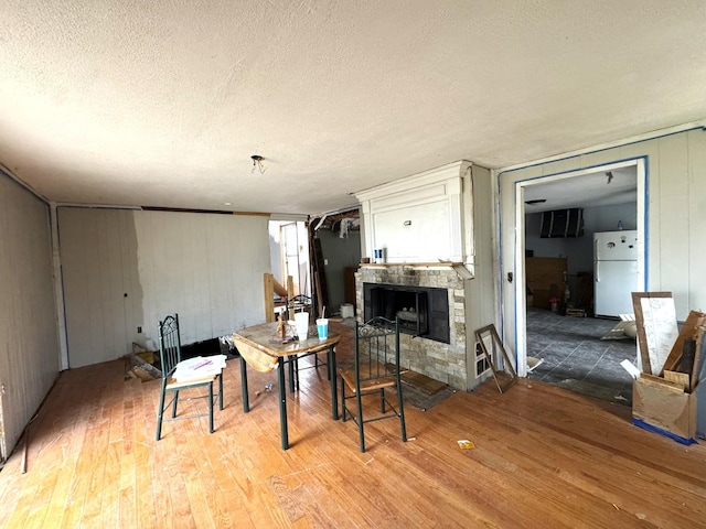 dining room featuring a stone fireplace, light wood-style floors, and a textured ceiling