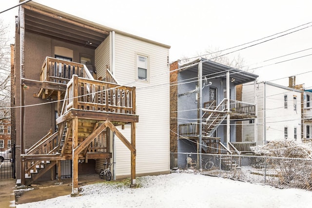snow covered house with brick siding, fence, and stairway