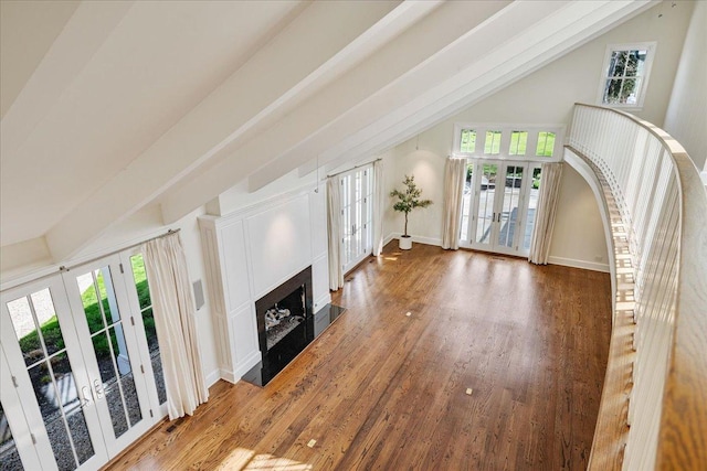 unfurnished living room with french doors, a fireplace, wood finished floors, and vaulted ceiling with beams