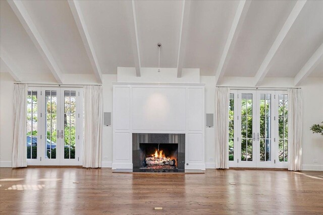 unfurnished living room featuring a healthy amount of sunlight, lofted ceiling with beams, french doors, and wood finished floors