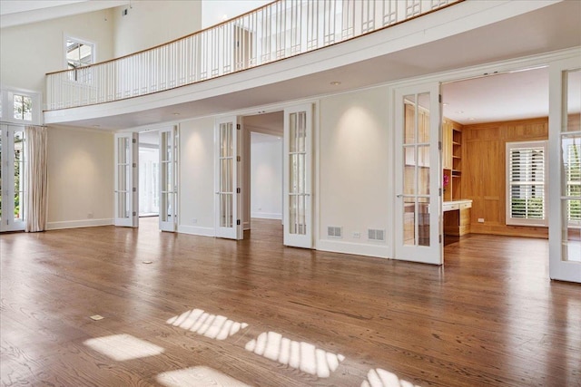 unfurnished living room with french doors, a towering ceiling, and wood finished floors