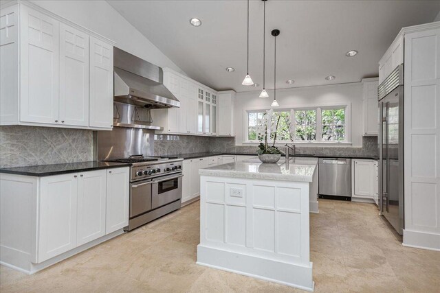 kitchen with high quality appliances, wall chimney exhaust hood, a center island, white cabinetry, and decorative backsplash
