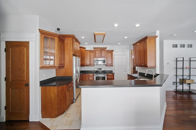 kitchen with a sink, dark countertops, appliances with stainless steel finishes, and a peninsula