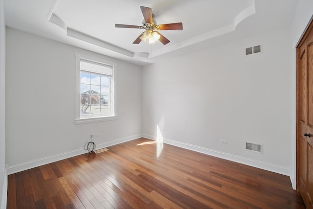 spare room featuring a tray ceiling, wood-type flooring, baseboards, ceiling fan, and visible vents