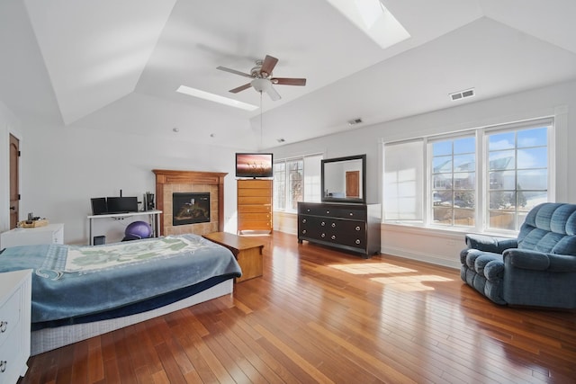 bedroom featuring a tray ceiling, a tiled fireplace, wood-type flooring, visible vents, and lofted ceiling with skylight