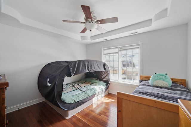 bedroom featuring hardwood / wood-style floors, a tray ceiling, baseboards, and visible vents