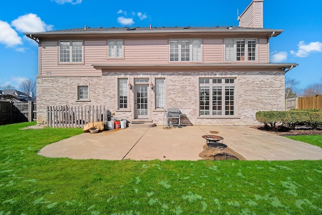 rear view of house featuring fence, a patio, brick siding, a yard, and a chimney