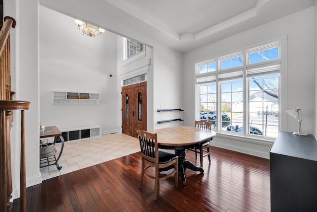 dining room featuring baseboards, a towering ceiling, dark wood finished floors, a tray ceiling, and an inviting chandelier