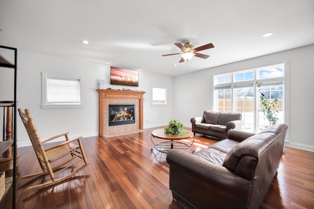 living room with baseboards, a tiled fireplace, ceiling fan, and hardwood / wood-style flooring