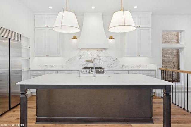 kitchen featuring light wood finished floors, light countertops, stainless steel built in fridge, and custom exhaust hood