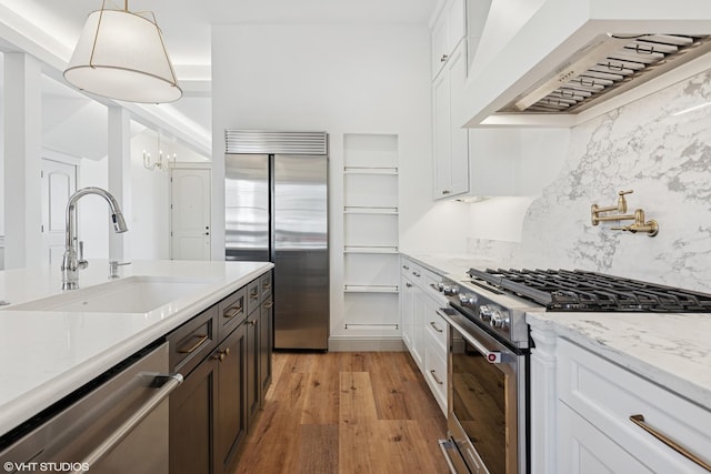 kitchen featuring a sink, custom range hood, high quality appliances, backsplash, and light wood-type flooring