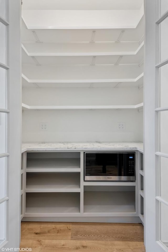 room details featuring open shelves, built in microwave, light wood-style flooring, and light stone countertops