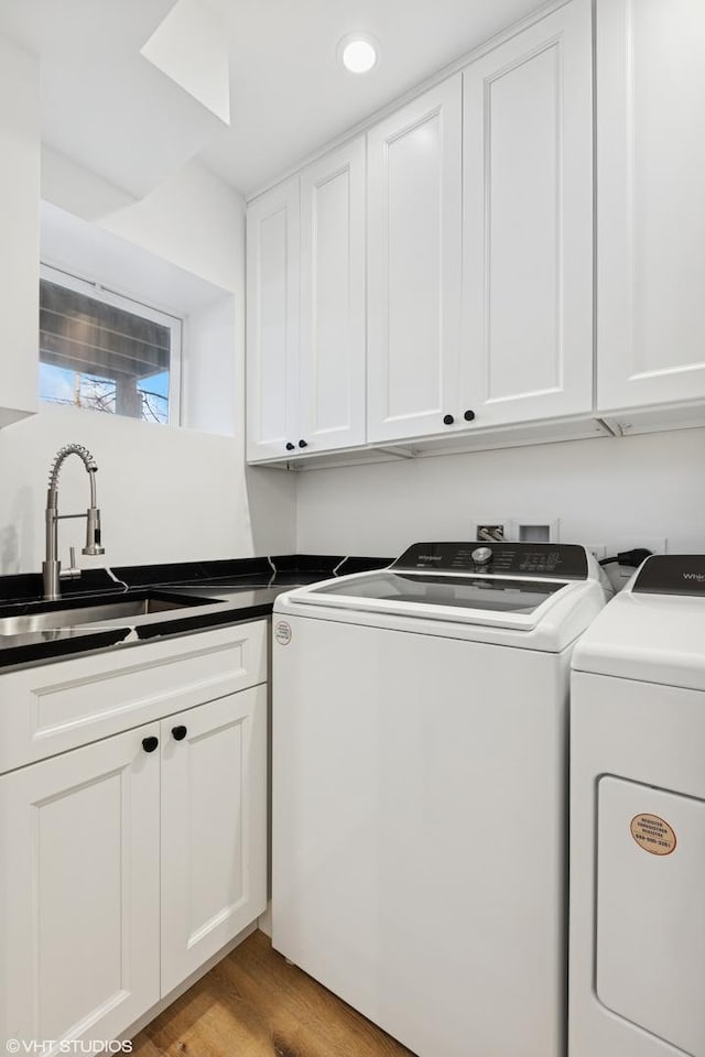 clothes washing area with a sink, washer and clothes dryer, cabinet space, and light wood finished floors