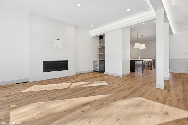 unfurnished living room featuring wine cooler, light wood-type flooring, recessed lighting, a fireplace, and baseboards