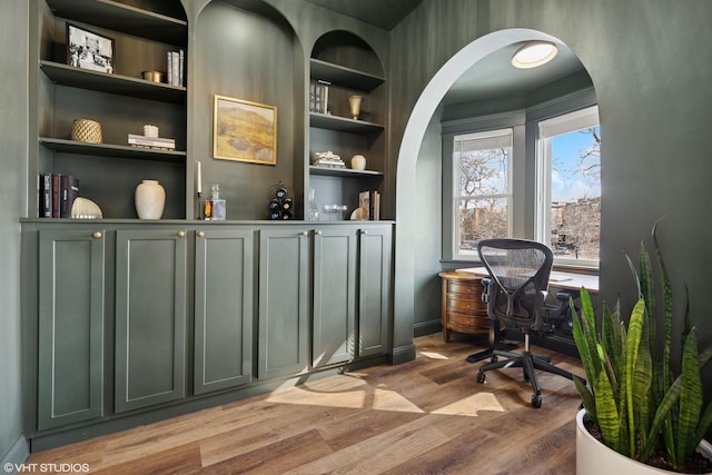 office featuring built in features, wood finished floors, baseboards, and arched walkways