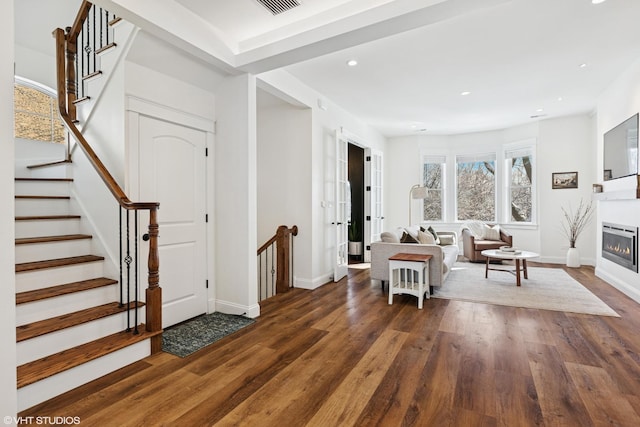 interior space with recessed lighting, baseboards, dark wood finished floors, a glass covered fireplace, and stairs
