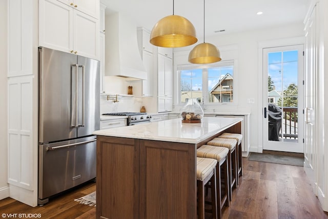 kitchen with high end appliances, dark wood-style flooring, a kitchen bar, white cabinets, and a kitchen island