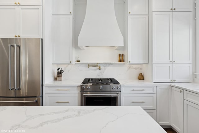 kitchen featuring tasteful backsplash, premium appliances, white cabinets, light stone countertops, and custom range hood