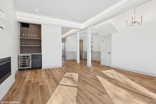 unfurnished living room with light wood finished floors, a bar, wine cooler, a chandelier, and recessed lighting