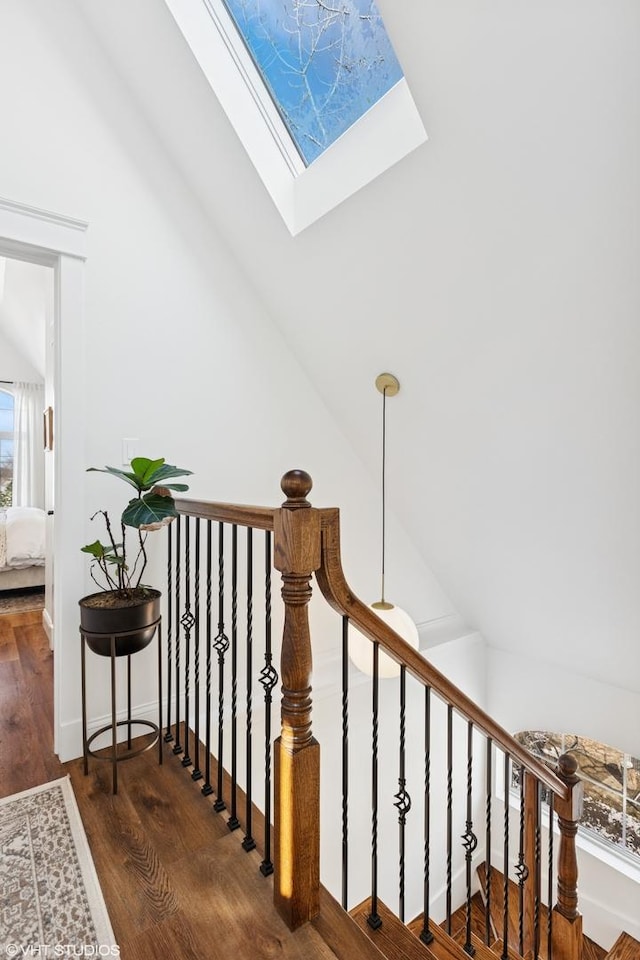 staircase with wood finished floors and vaulted ceiling with skylight