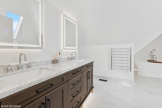bathroom with double vanity, visible vents, a freestanding bath, and a sink