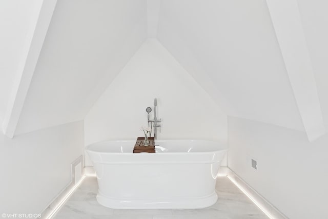 bathroom with a soaking tub, lofted ceiling, baseboards, and marble finish floor