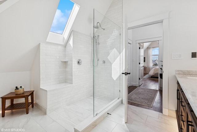 ensuite bathroom with connected bathroom, vanity, lofted ceiling with skylight, and a tile shower