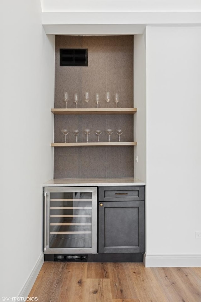 bar with a bar, visible vents, baseboards, light wood-style floors, and wine cooler