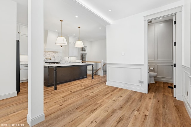 kitchen with premium range hood, decorative backsplash, light countertops, white cabinets, and light wood-type flooring