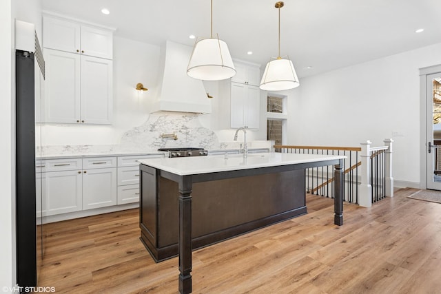 kitchen featuring light wood finished floors, a sink, light countertops, custom range hood, and recessed lighting