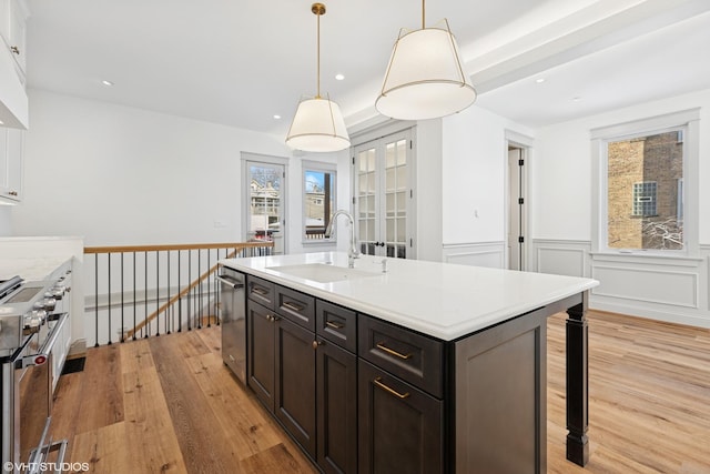 kitchen featuring light wood-style flooring, stainless steel appliances, a sink, a wainscoted wall, and light countertops
