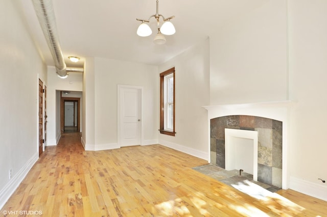 unfurnished living room featuring a chandelier, light wood-style floors, a tiled fireplace, and baseboards