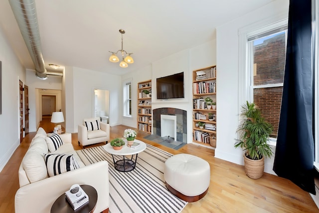 living room with a notable chandelier, baseboards, built in shelves, wood finished floors, and a tile fireplace