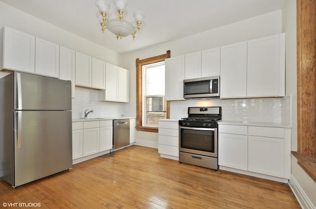 kitchen featuring stainless steel appliances, a notable chandelier, light wood-style flooring, and white cabinets