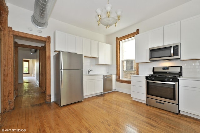kitchen with a sink, light wood-type flooring, a chandelier, light countertops, and appliances with stainless steel finishes
