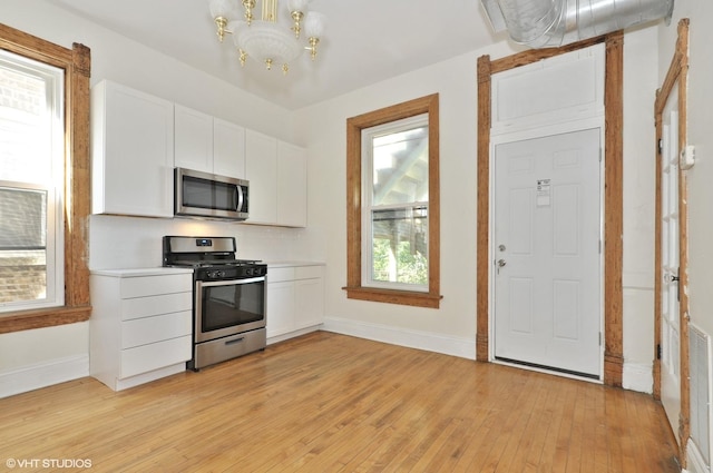 kitchen featuring baseboards, light wood finished floors, an inviting chandelier, stainless steel appliances, and white cabinets
