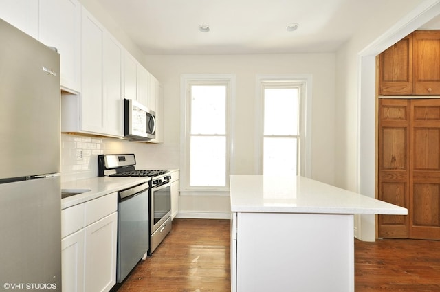 kitchen featuring dark wood finished floors, backsplash, light countertops, a kitchen island, and appliances with stainless steel finishes