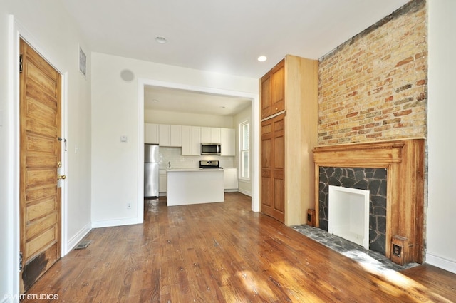 unfurnished living room with dark wood-type flooring, a fireplace, baseboards, and visible vents