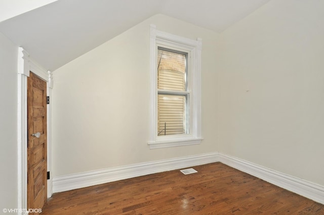 additional living space with wood finished floors, a wealth of natural light, visible vents, baseboards, and vaulted ceiling