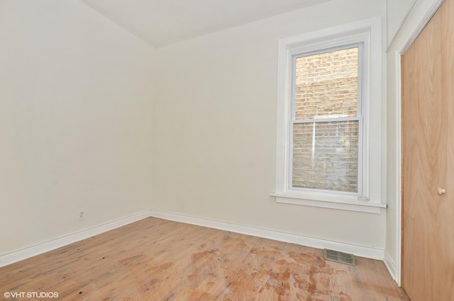 spare room with light wood-type flooring, visible vents, and baseboards
