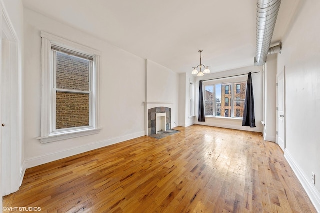 unfurnished living room featuring a fireplace, a chandelier, baseboards, and light wood-type flooring