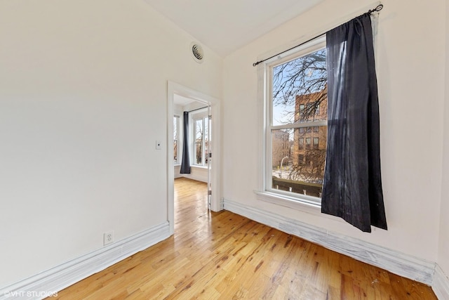empty room featuring lofted ceiling, light wood-style flooring, and baseboards