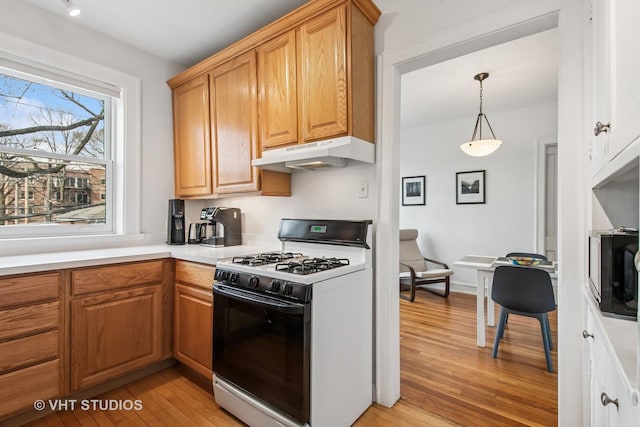 kitchen with light wood finished floors, under cabinet range hood, light countertops, gas stove, and hanging light fixtures