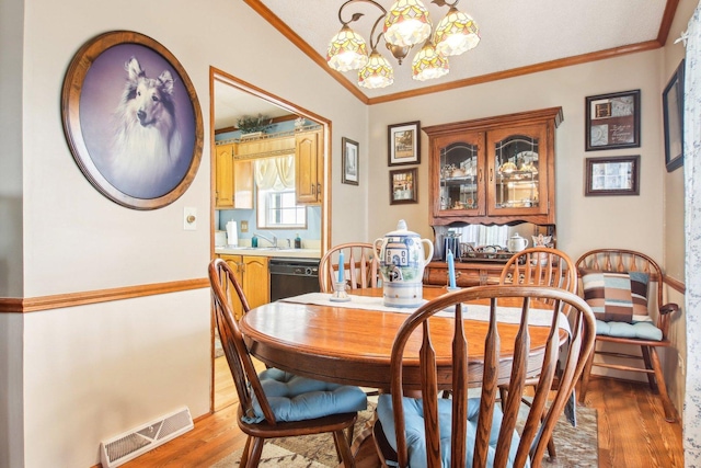 dining room with visible vents, ornamental molding, light wood-style flooring, and a chandelier