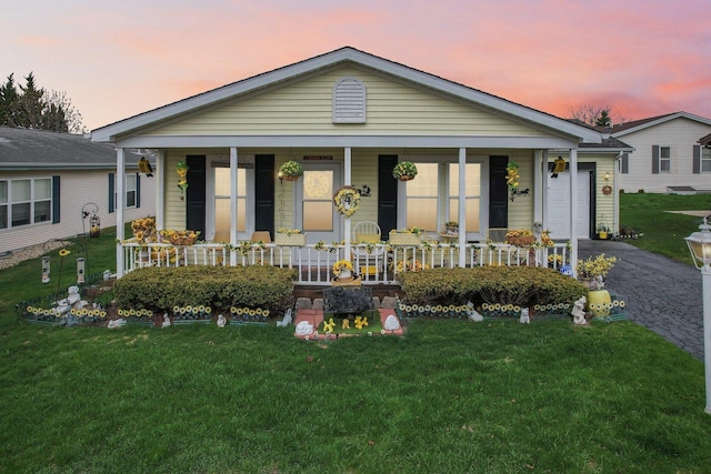 view of front of home featuring covered porch, an attached garage, driveway, and a front yard