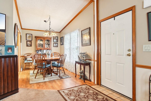 dining room featuring crown molding, a textured ceiling, a chandelier, light wood-style flooring, and vaulted ceiling