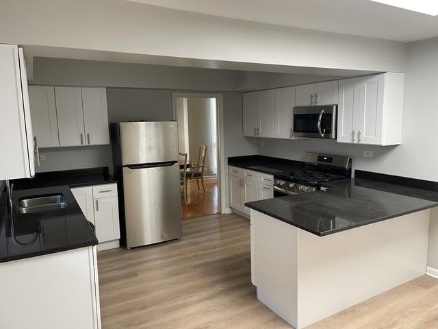 kitchen with a sink, dark countertops, light wood-style flooring, and appliances with stainless steel finishes