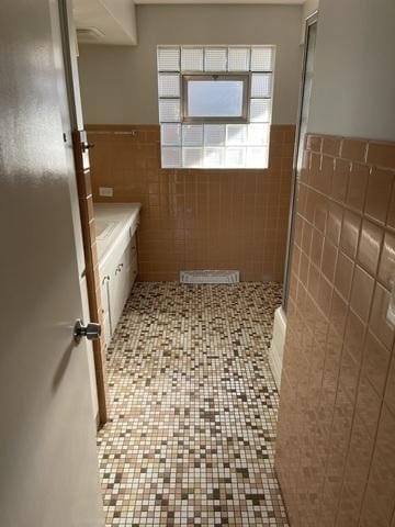 bathroom with tile walls, a stall shower, tile patterned flooring, and wainscoting