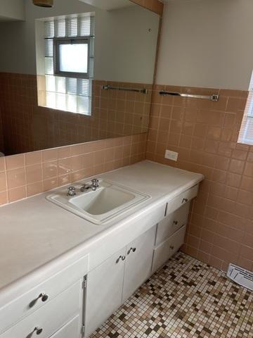 bathroom with a wainscoted wall, vanity, tile patterned flooring, visible vents, and tile walls