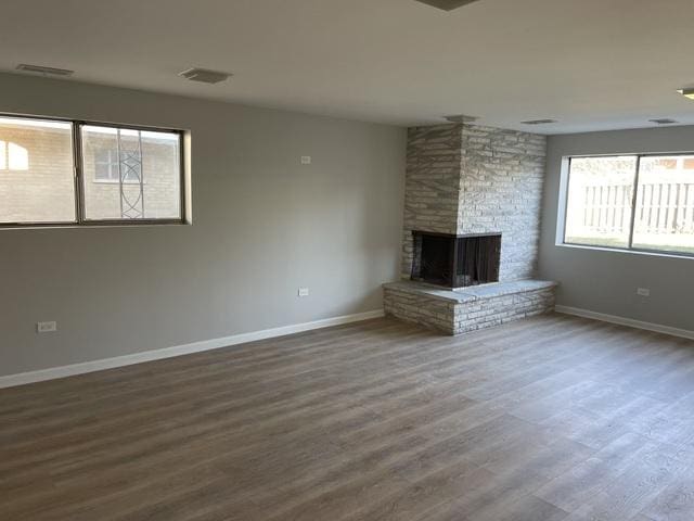 unfurnished living room with baseboards, visible vents, wood finished floors, and a multi sided fireplace